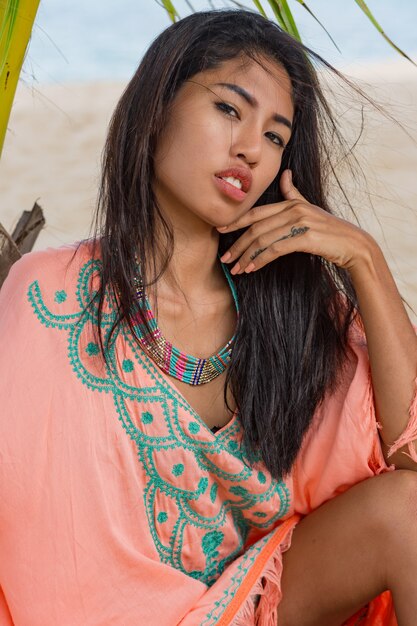 Открытый модный портрет азиатской женщины на тропическом пляже, она расслабляется, мечтает. Ношение украшений, браслета и ожерелья.