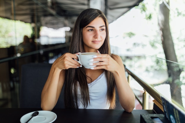 Outdoor fashion portrait of beautiful girl drinking tea coffee alone