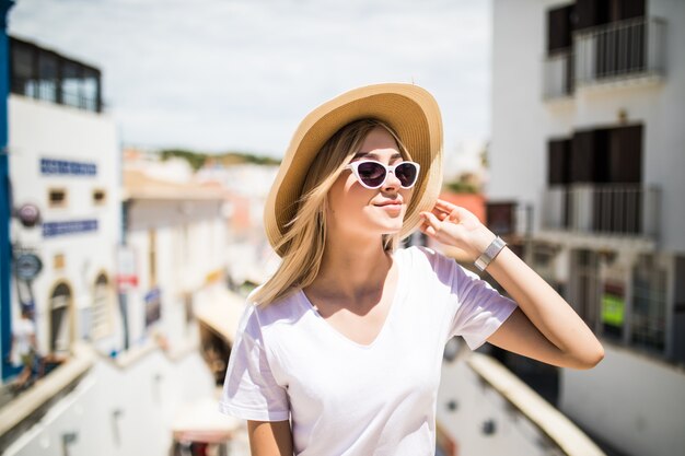 Outdoor fashion portrait girl wearing hat, trendy sunglasses sitting on handrail
