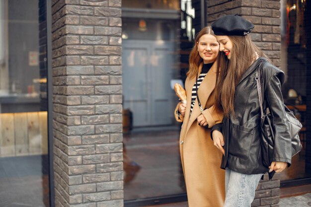 Открытый модный портрет двух молодых красивых женщин в модной стильной одежде. Молодые девушки позируют на улице европейского города. Девушки идут по улице.