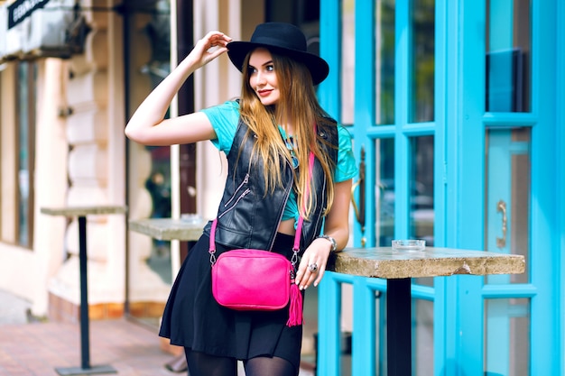Outdoor lifestyle fashion portrait of pretty blonde woman walking and enjoy summer sunny day,stylish outfit, mini skirt, vintage hat, biker jacket, bright details and accessorizes, europa city center