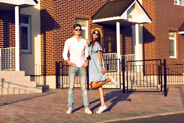 Outdoor lifestyle portrait of pretty young couple on romantic date having fun together, hugs and kisses, posing on the street, travel together, family portrait.