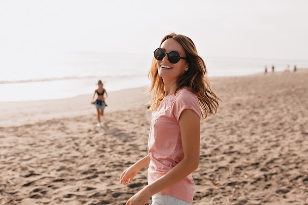 Outdoor photo of happy young female model in summer t-shirt standing against blue sky and sandy beach Woman having fun out on a summer day