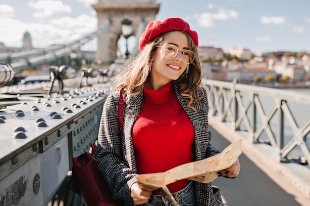 Free photo outdoor photo of pretty female traveler in glasses holding map on the city bridge