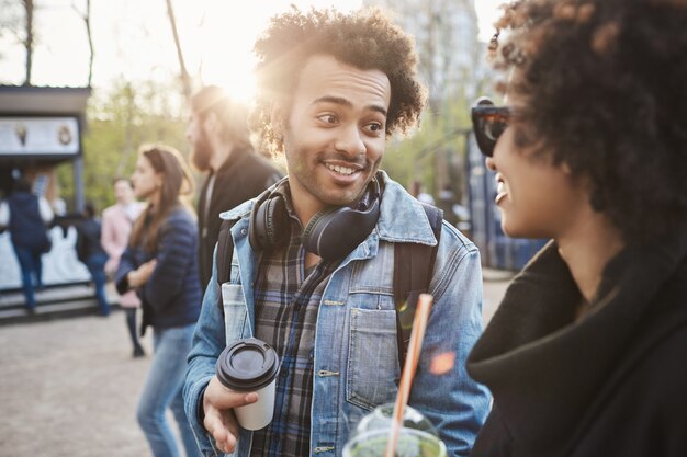 トレンディな服を着て話したり、コーヒーを飲みながら公園を歩いているアフリカ系アメリカ人の友人の屋外のポートレート。