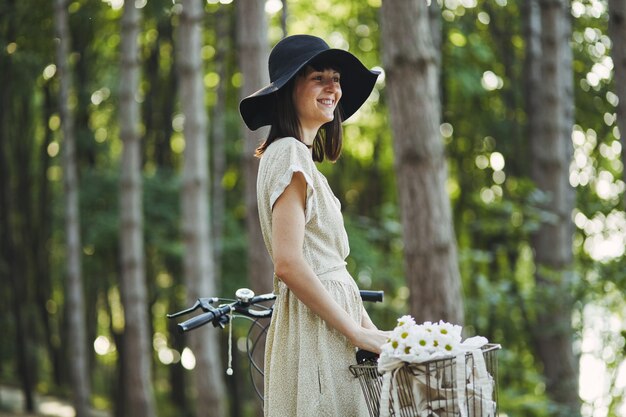 Outdoor portrait of attractive young brunette in a hat on a bicycle.