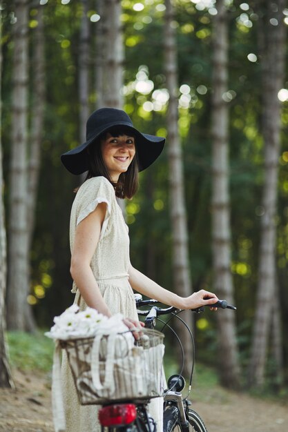 自転車に乗って帽子の魅力的な若いブルネットの屋外のポートレート。