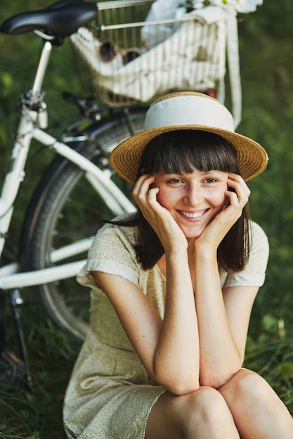 Ritratto all'aperto di giovane castana attraente in un cappello su una bicicletta.