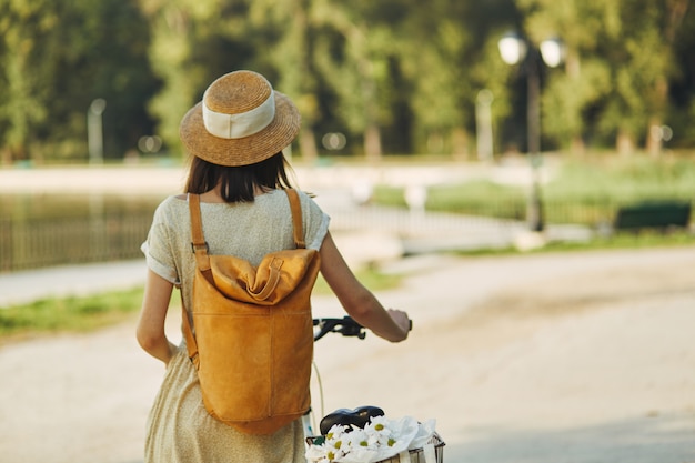 Outdoor portrait of attractive young brunette in a hat on a bicycle.