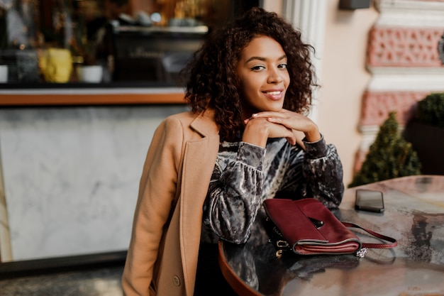 Free photo outdoor  portrait of  beautiful  smiling black woman with stylish afro hairs sitting in cafe in paris.