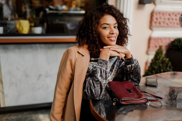 Outdoor  portrait of  beautiful  smiling black woman with stylish afro hairs sitting in cafe in Paris.