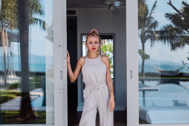 Outdoor portrait of caucasian woman in classic jumpsuit with red lipstick on vacation outside villa hotel