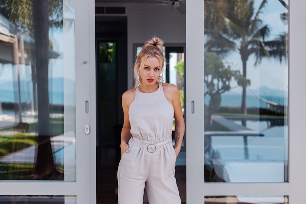 Outdoor portrait of caucasian woman in classic jumpsuit with red lipstick on vacation outside villa hotel