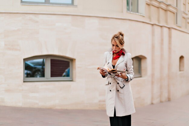 Outdoor portrait of disappointed european woman in long coat standing on the street and looking down