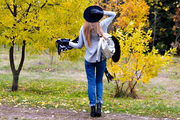 Outdoor portrait of excited girl wears trendy broad-brim and standing in confident pose. Attractive young woman in glasses posing on autumn nature background.