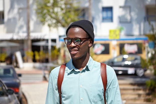 세련 된 의류 도시 속에서 걷고 유행 젊은 아프리카 계 미국인 학생의 야외 초상화, 발로 대학에가는 동안 화창한 아침을 즐기고, 그의 얼굴에 쾌활한 표정