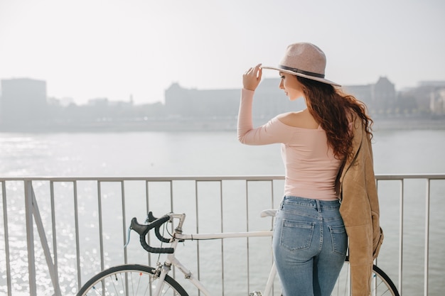 Outdoor portrait from back of romantic long-haired woman enjoying city views in morning