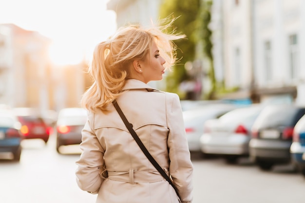 Outdoor portrait from back of serious lady in beige coat looking away standing on the street