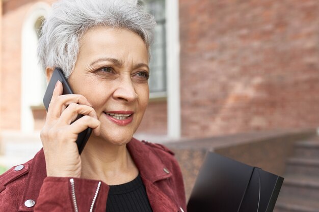 Outdoor portrait of good looking confident middle aged business woman speaking on mobile