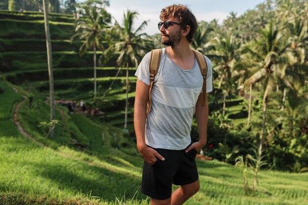 Outdoor portrait of Handsome travel man with back pack walking on rise terrace in Bali.