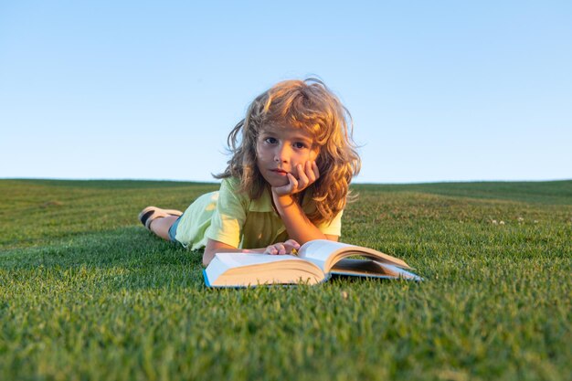 Уличный портрет милого маленького мальчика, читающего книгу, школьника с книгой, отдыхающего на свежем воздухе