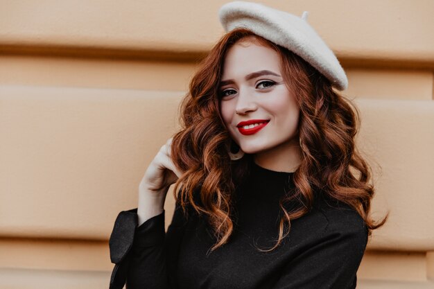 Outdoor portrait of pleasant caucasian woman with long ginger hair. Adorable french model in beret smiling.