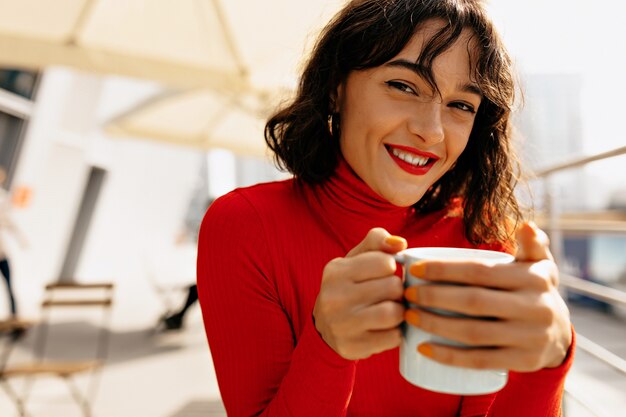 Ritratto all'aperto di giovane donna attraente sorridente con capelli scuri ricci corti e labbra rosse