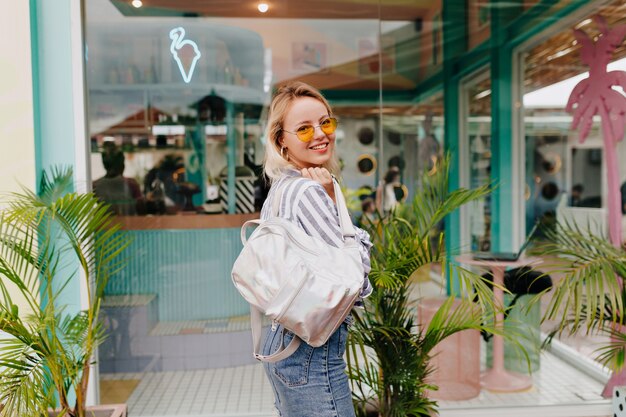 Outdoor portrait of stylish pretty woman wearing stripped shirt and round orange glasses