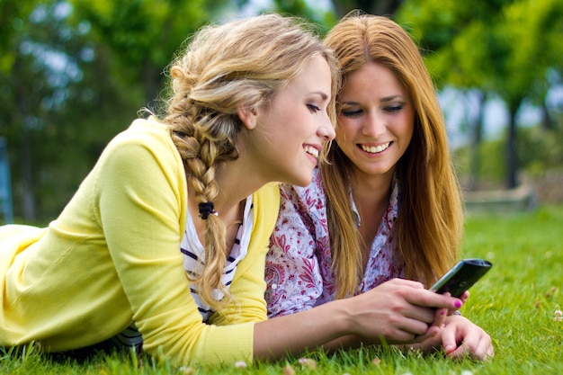 Открытый Портрет двух красивых молодых женщин с мобильного в парке