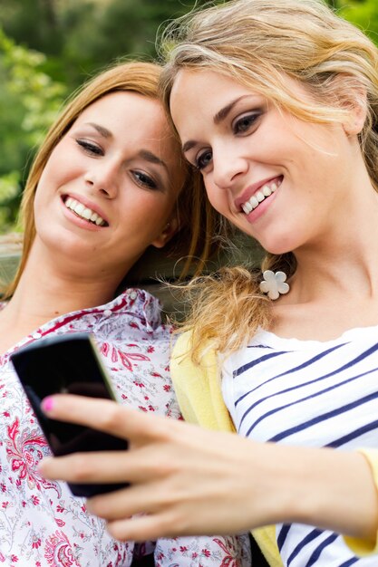 Outdoor Portrait of two beautiful young womens with mobile at the park