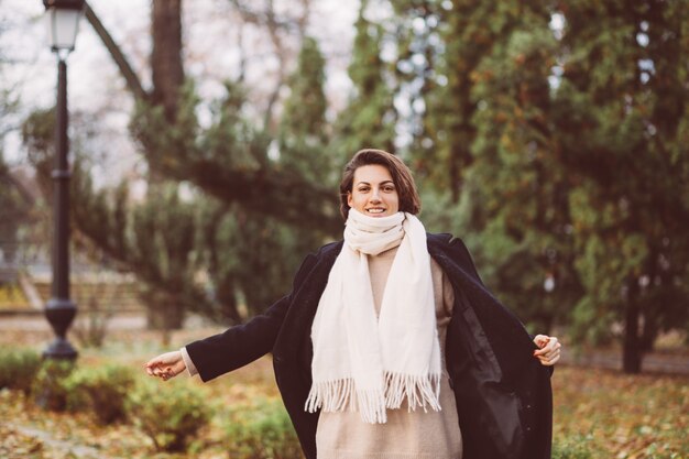 Outdoor portrait of woman in park wearing winter black coat and white scarf