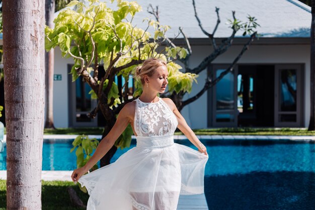 Outdoor portrait of woman in white wedding dress at villa in sunny day, tropical view