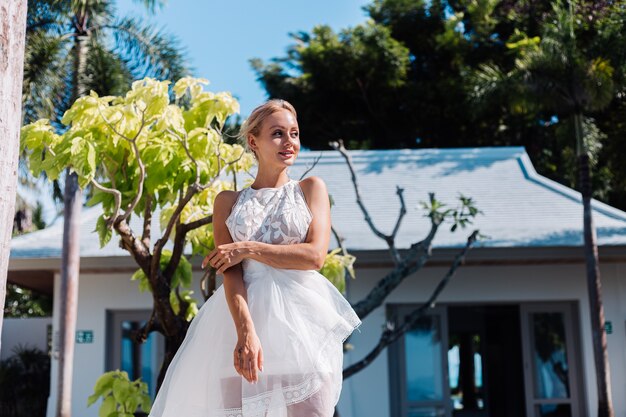 Открытый портрет женщины в белом свадебном платье на вилле в солнечный день, тропический вид