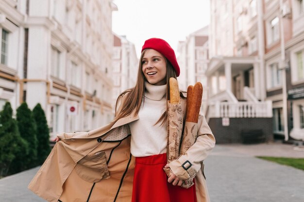 Outdoor portrait of young attractive woman in French outfit is posing on european old street with bagels