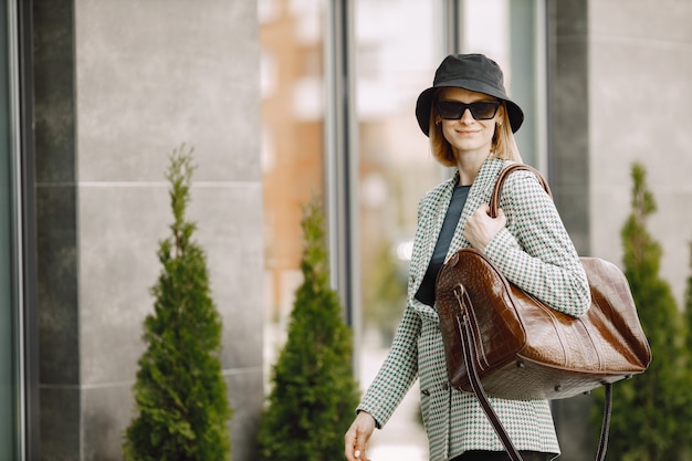 Free photo outdoor portrait of a young beautiful fashionable woman walking on the street, holding big brown leather bag. model wearing stylish clothes