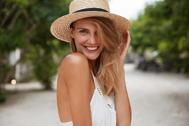 Outdoor shot of good looking young happy female with broad shining smile, wears summer stylish clothing