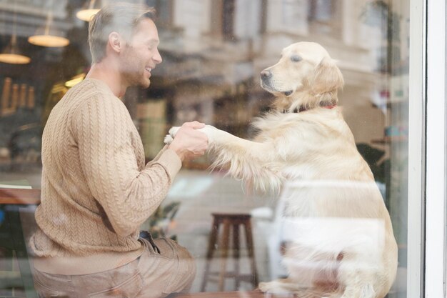 An outdoor shot of a man sitting with his dog in a petfriendly cafe near window golden retriever