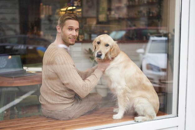 Foto gratuita una foto all'aperto di un caffè per animali domestici dove un uomo si siede vicino alla finestra con il suo peloso golden retriever