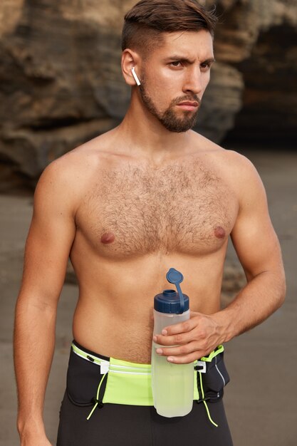 Outdoor shot of self confident male lover of sport, has morning workout at coastline