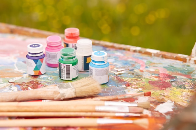 Outdoor shot of various containers for paint and professional brushes situated on dirty palette