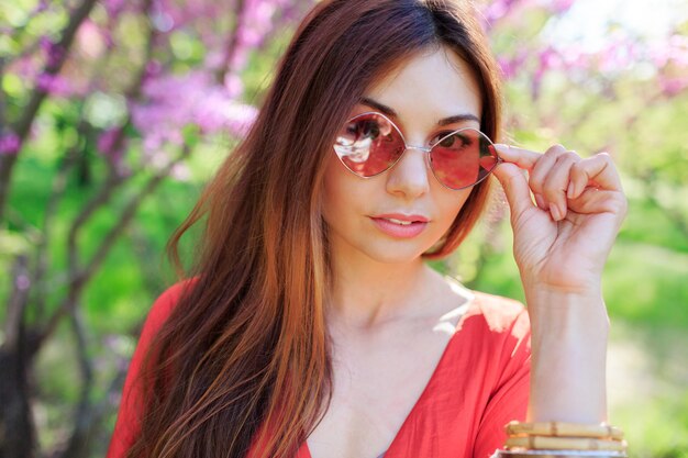 Outdoor spring close up portrait of brunette woman enjoying flowers in sunny blooming garden.