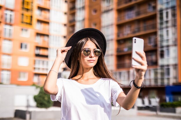 세련 된 hipster 모자를 쓰고 거리에 selfie를 만드는 젊은 유행 여자의 야외 거리.