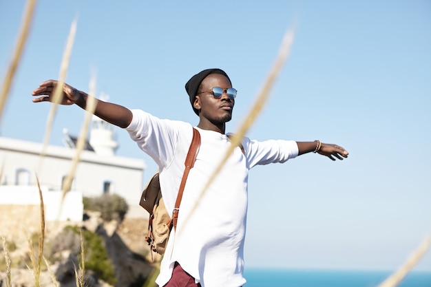 Free photo outdoor summer shot of carefree happy young traveler standing at seaside with arms outstretched