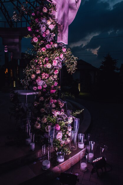 Outdoors composition made of roses and greenery with candles illuminated in the night