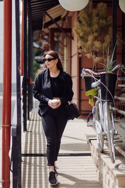 Free photo outdoors lifestyle portrait of stunning brunette girl. drinking coffee and walking on the city street.