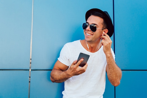 Outdoors photo of attractive guy in sunglasses listening to music in earphones