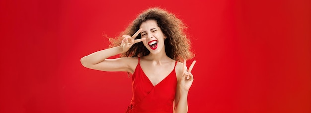 Free photo outgoing friendly and carefree young rebellious woman with curly hairstyle in red stylish dress show