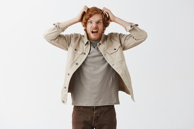 Outraged bearded redhead guy posing against the white wall