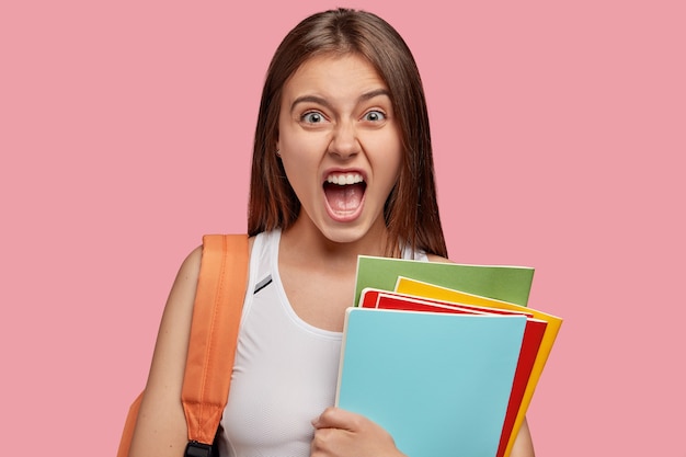 Outraged brunette woman exclaims with fury, keeps mouth widely opened, feels irritated with lazy groupmate