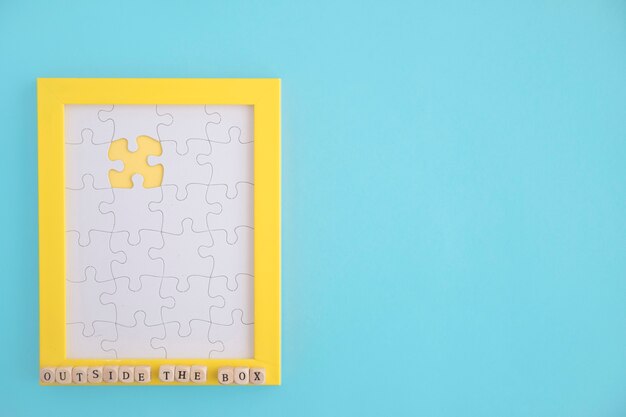 Outside the box puzzle yellow frame with white jig jaw pieces over the blue background